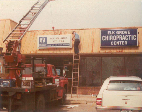 A worker on a ladder installs a sign on a building with 