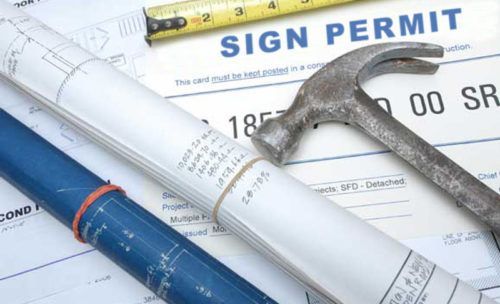 Construction documents, sign permit, hammer, and measuring tape, illustrating construction and permits.