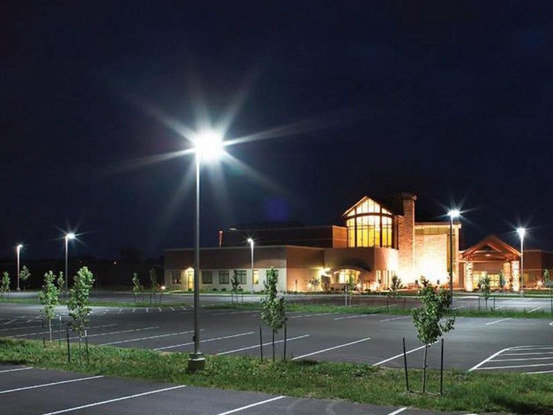 Night view of a parking lot lit by streetlights in front of a building with warm interior lighting.