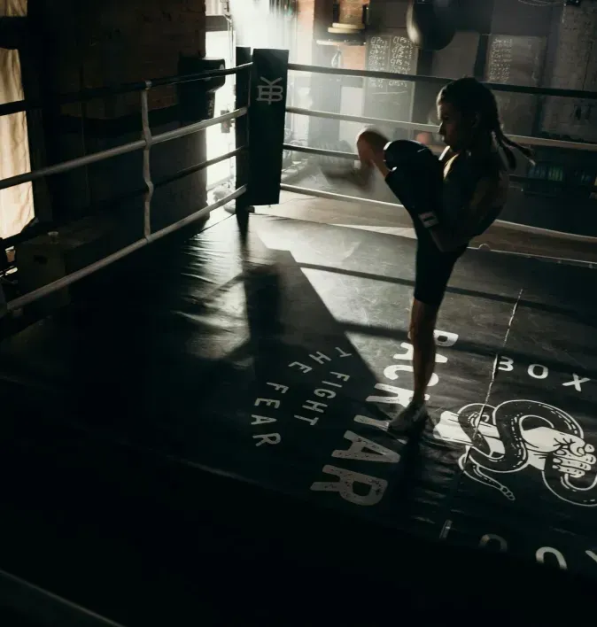 A woman is kicking a boxing ring in a gym.