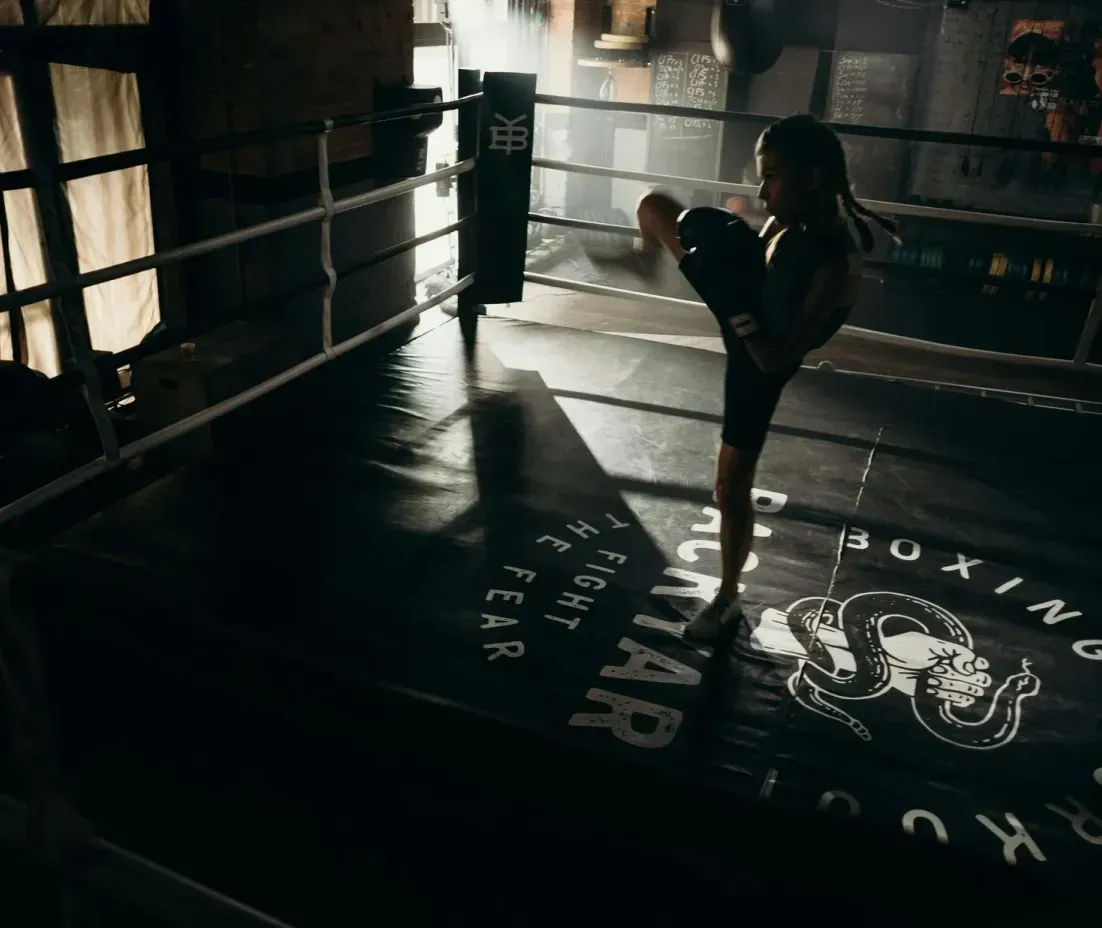 A woman is kicking a boxing ring in a gym.