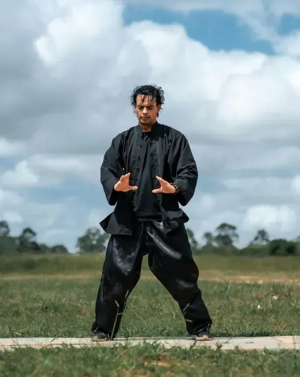 A man in a black karate uniform is standing in a field.