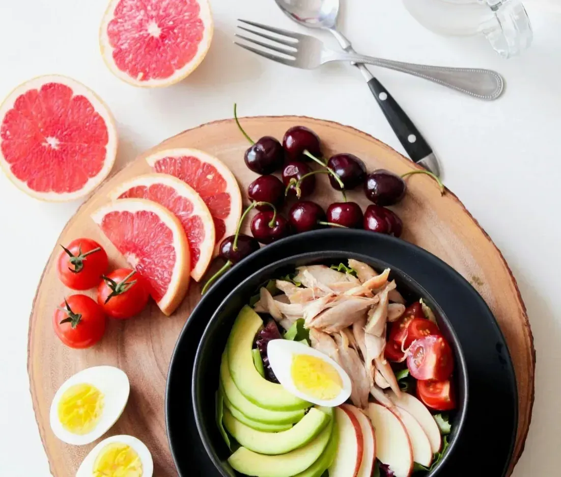 A bowl of food with eggs , avocado , grapefruit and cherries on a wooden cutting board.