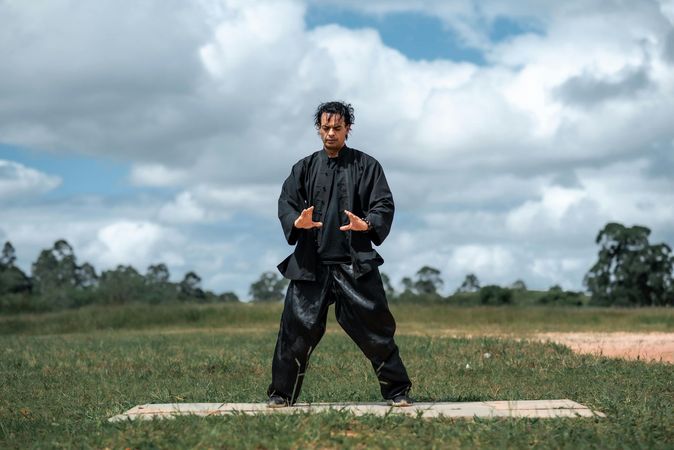 A man in a black karate uniform is standing in a field.