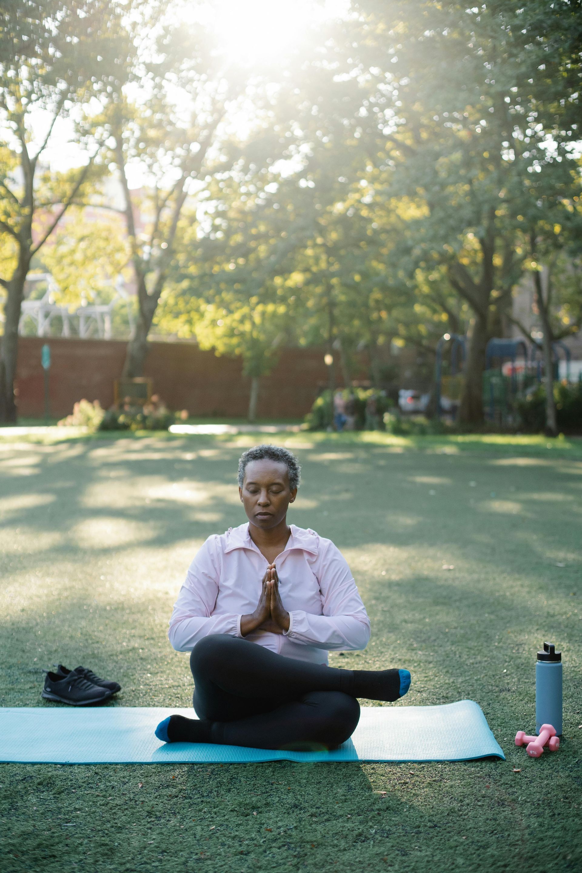 A woman is sitting on a yoga mat in a park.