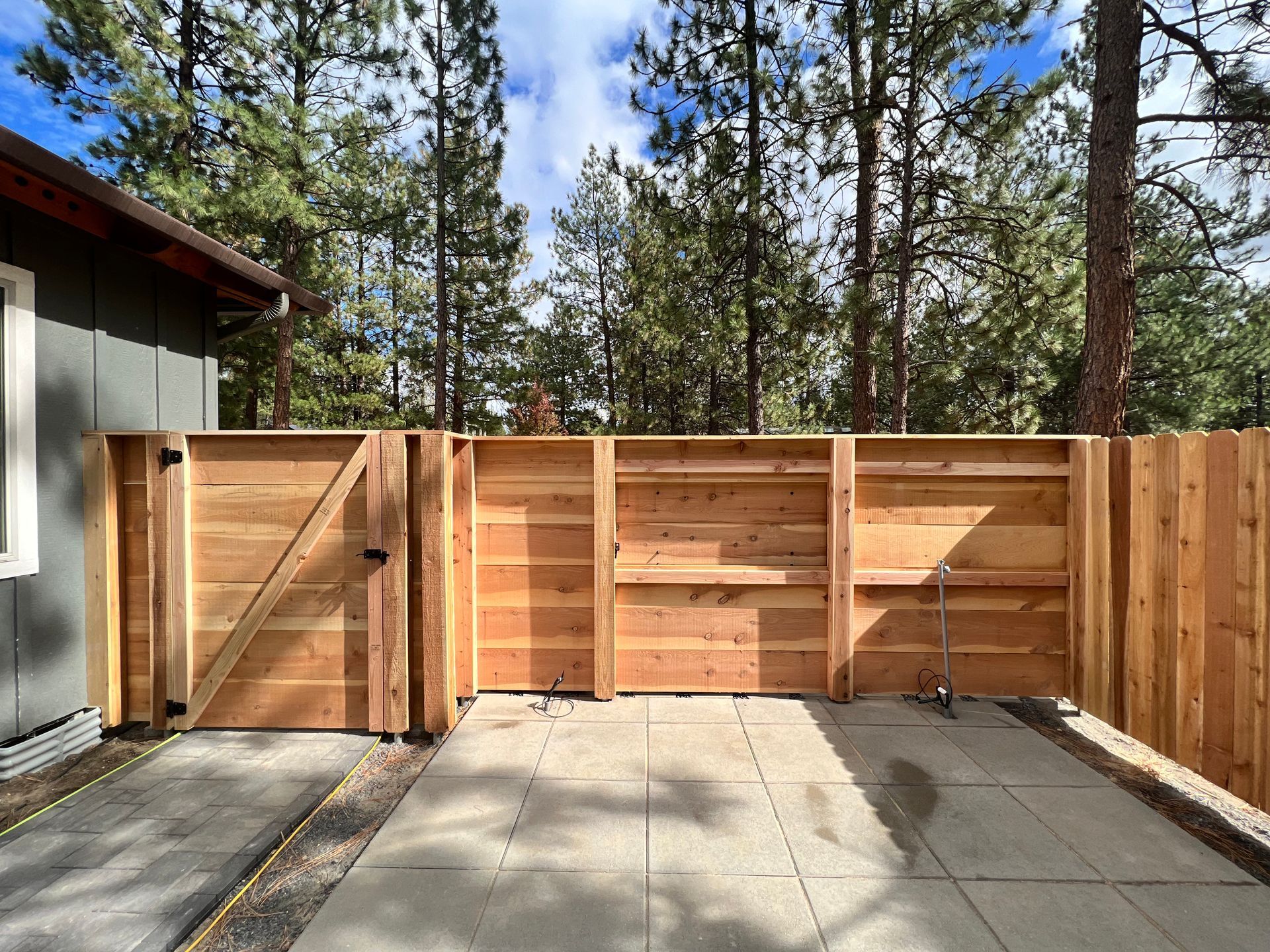 A wooden fence is surrounding a patio with trees in the background.