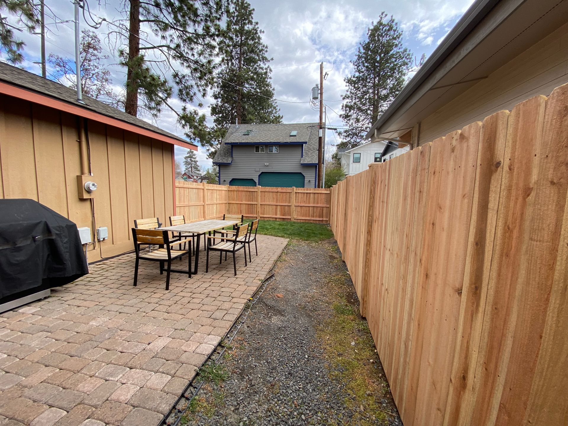 A wooden fence surrounds a patio area with a table and chairs.