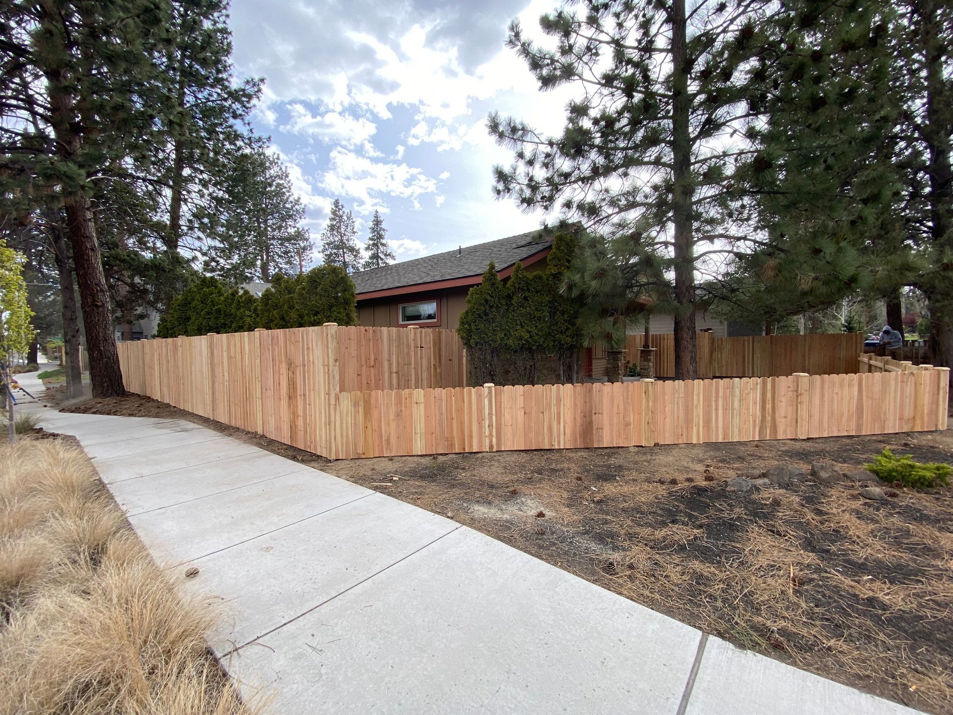 A wooden fence is along the side of a sidewalk in front of a house.