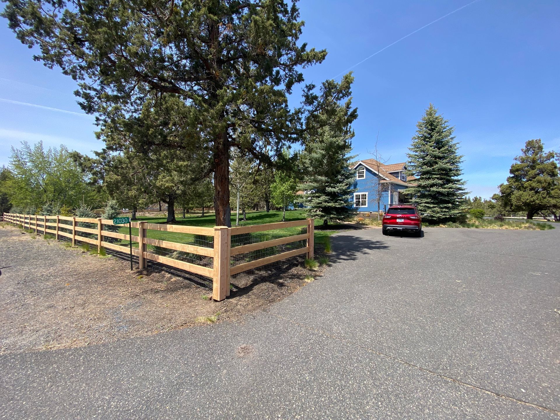 A red car is parked in front of a blue house behind a wooden fence.