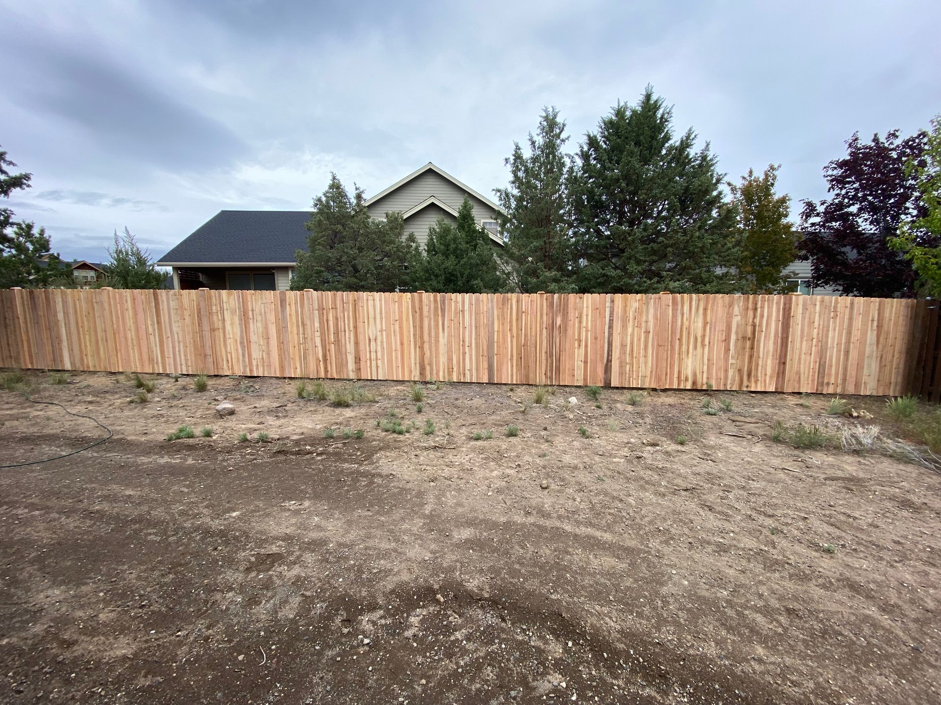 A wooden fence surrounds a dirt field in front of a house.