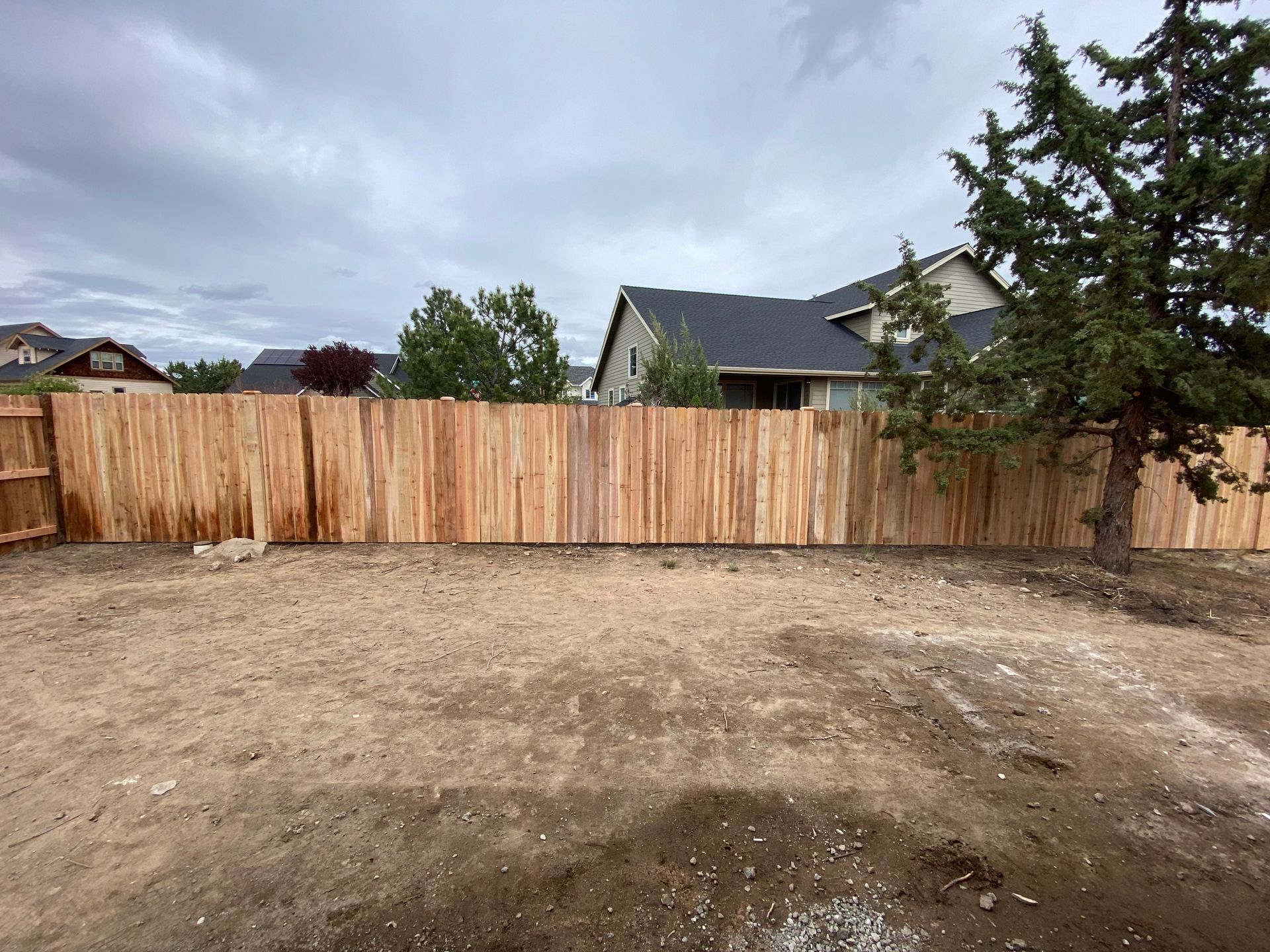 A wooden fence surrounds a dirt field in front of a house.