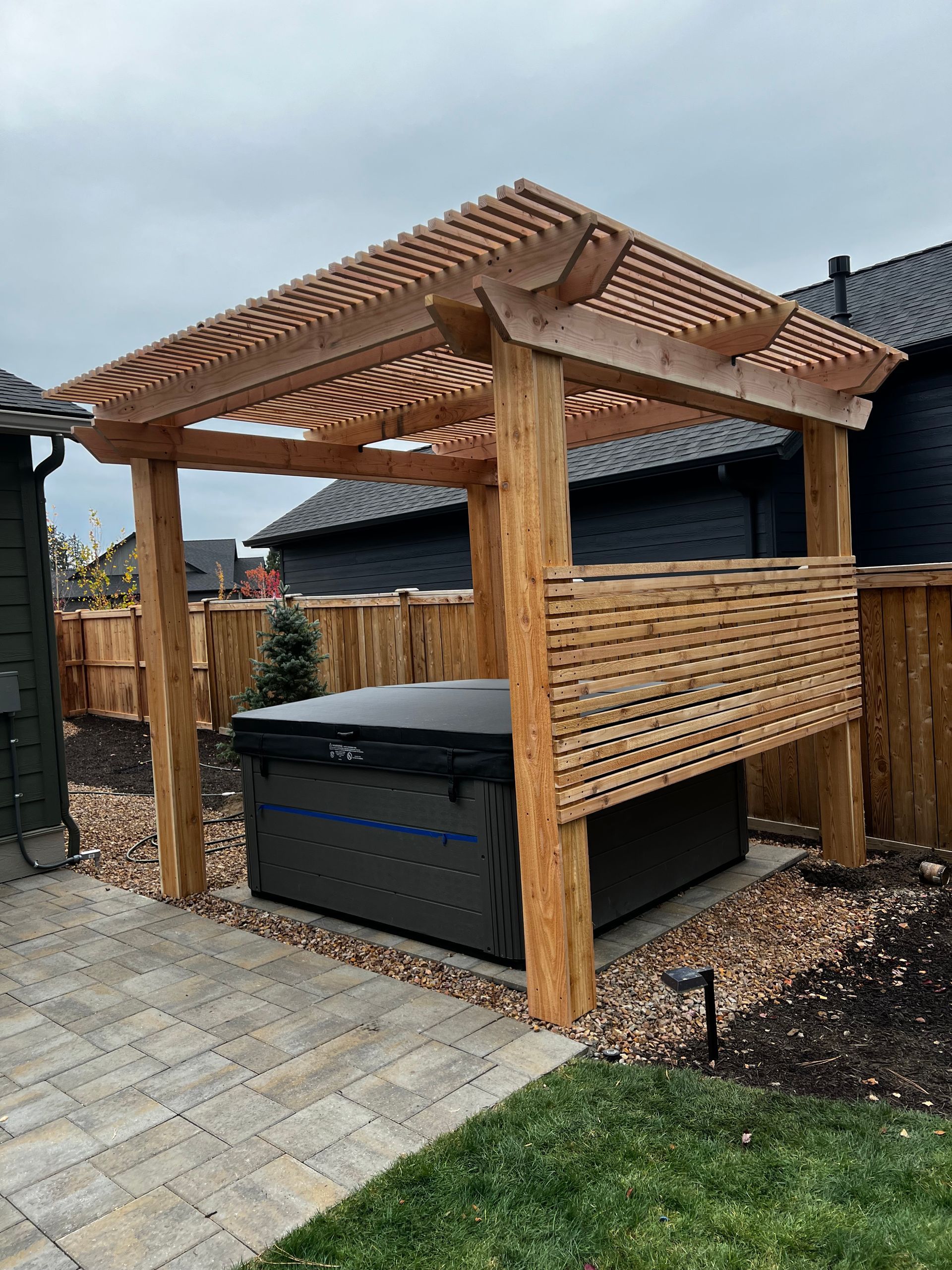 A hot tub is under a wooden pergola in a backyard.