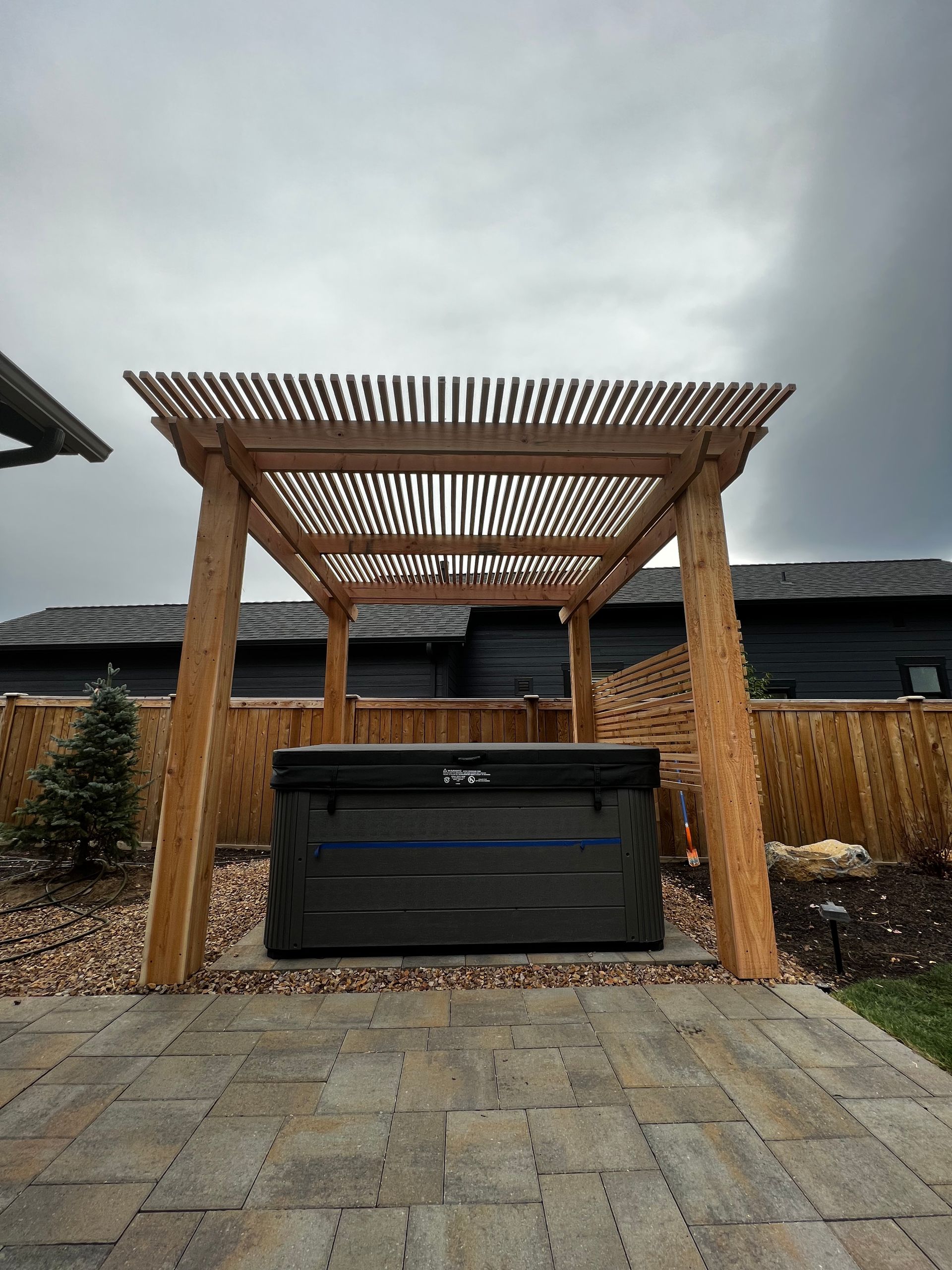 A hot tub is under a wooden pergola on a patio.