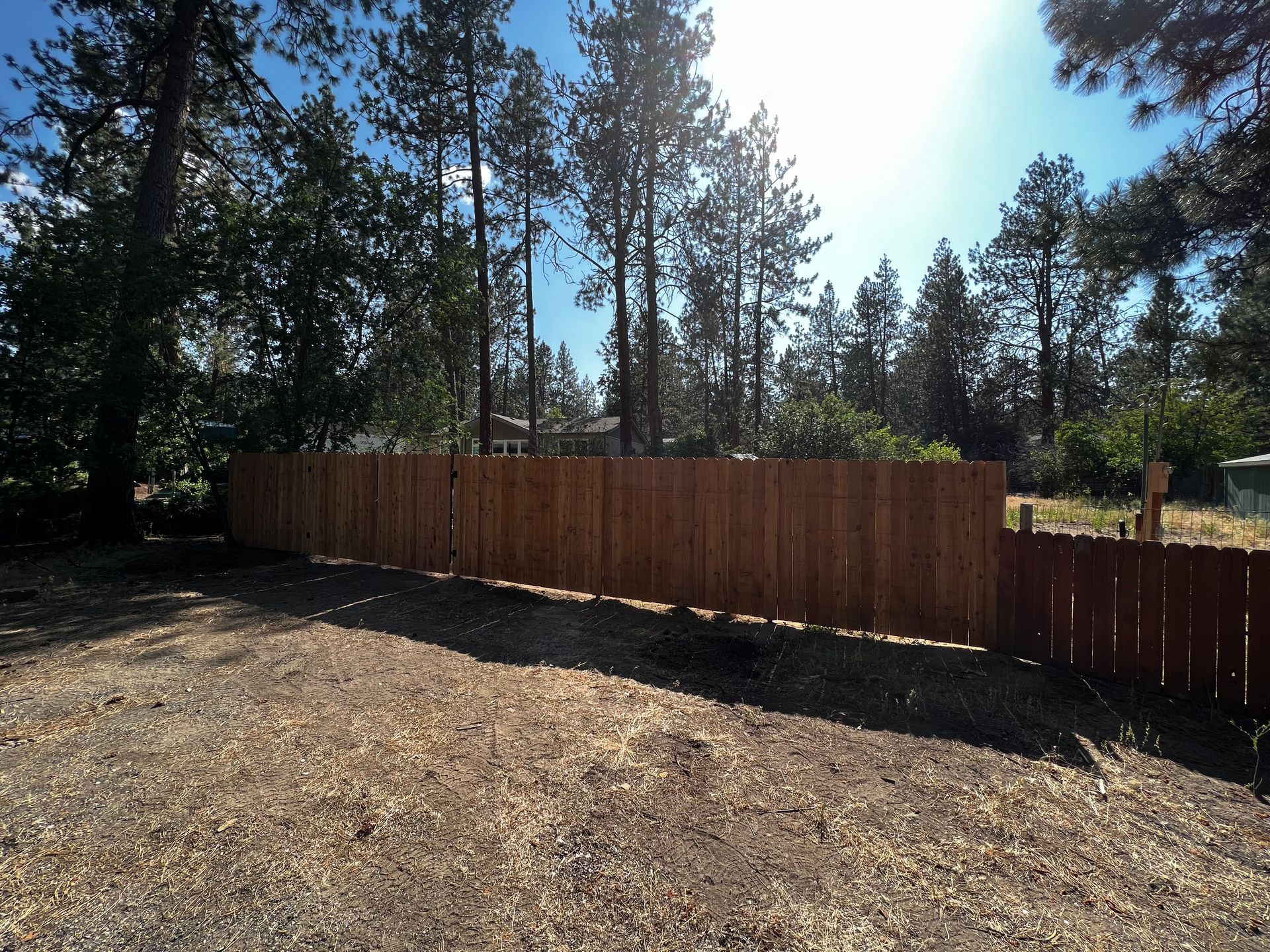 A wooden fence surrounds a dirt field with trees in the background
