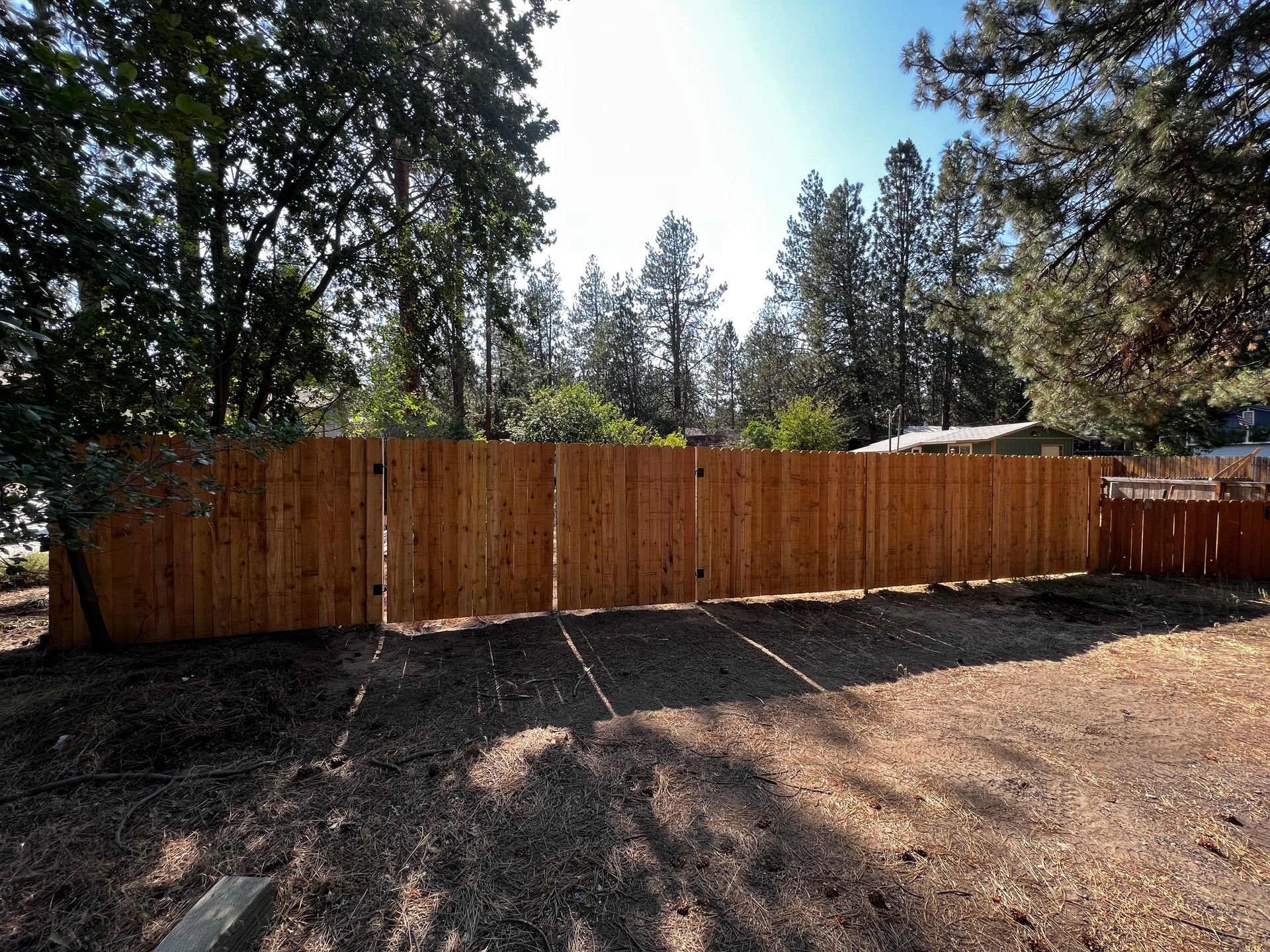 A wooden fence surrounds a yard with trees in the background