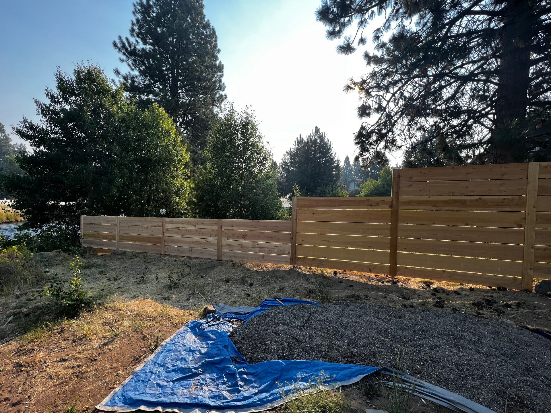 A wooden fence surrounds a gravel yard with trees in the background.