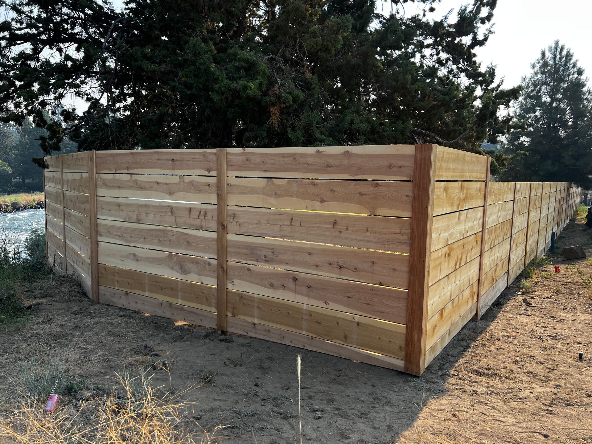 A wooden fence is sitting on top of a dirt field next to a river.