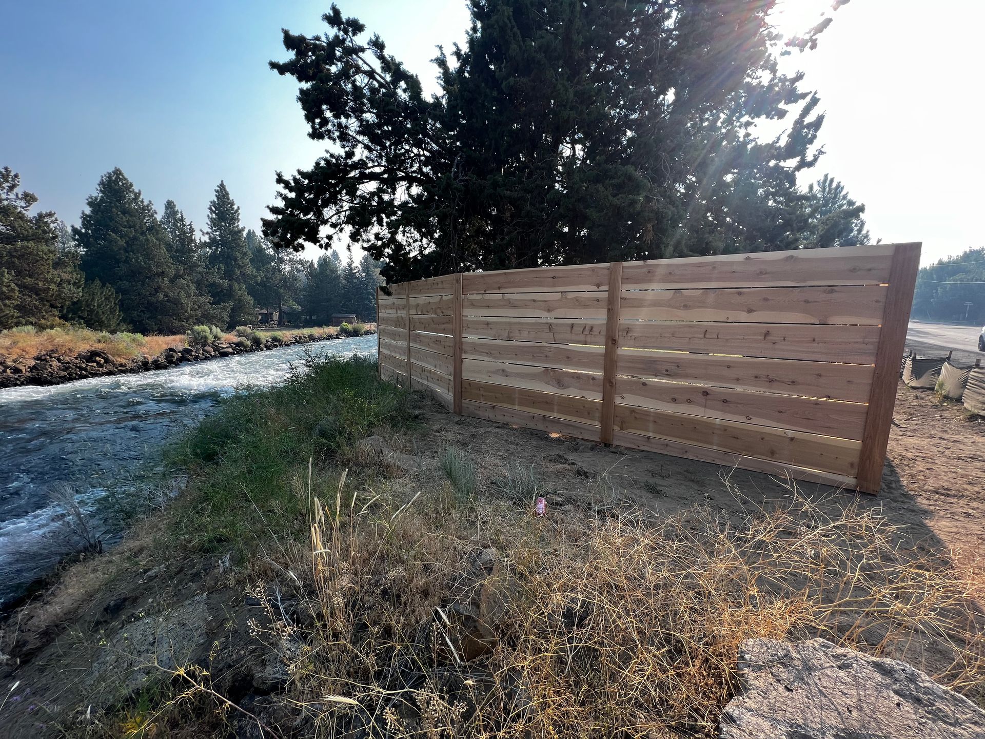 A wooden fence along a river with trees in the background