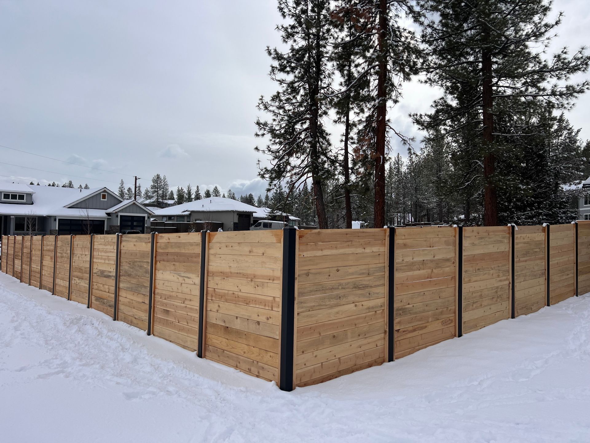 A wooden fence is surrounded by snow and trees