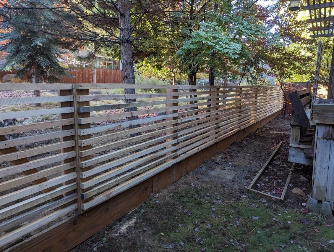 A wooden fence is surrounded by trees in a backyard.