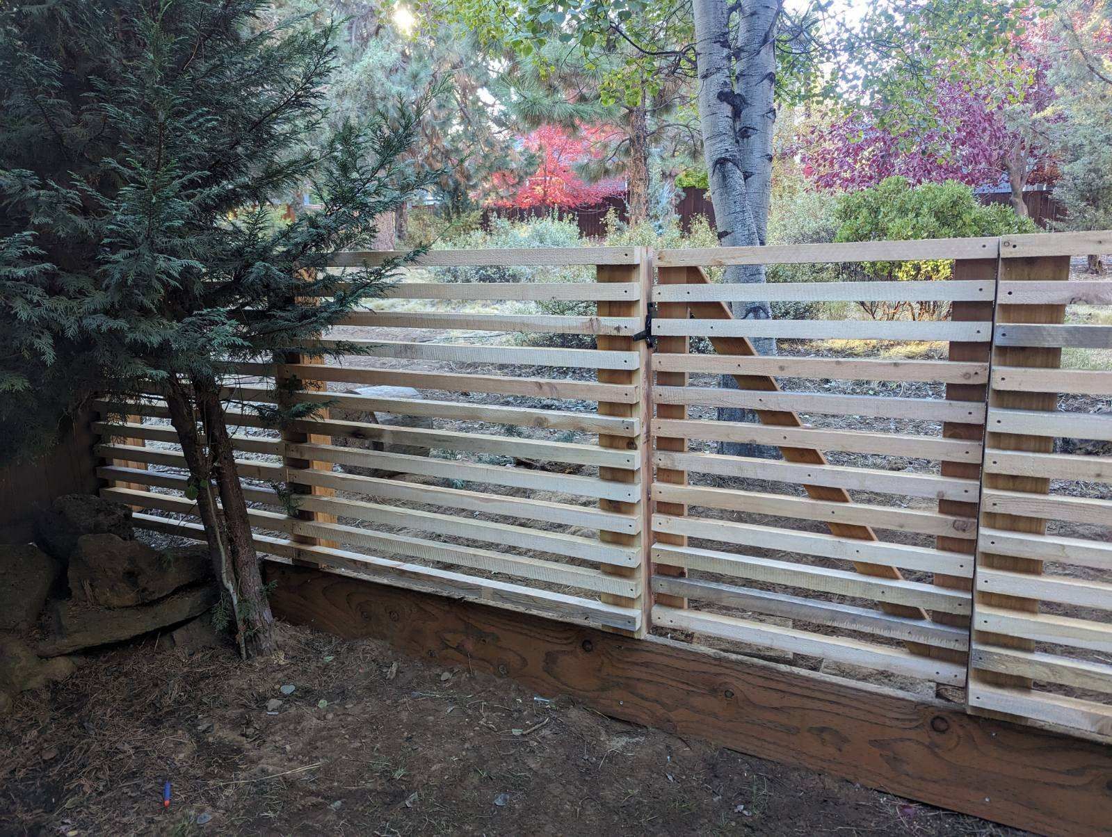 A wooden fence made out of pallets is surrounded by trees.