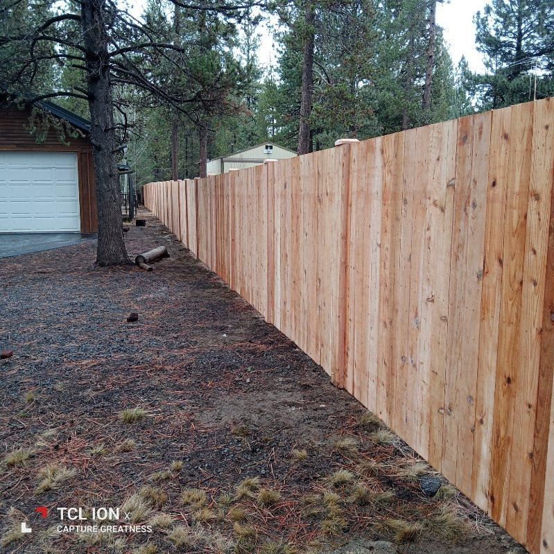 A wooden fence is surrounded by trees and grass in front of a garage.