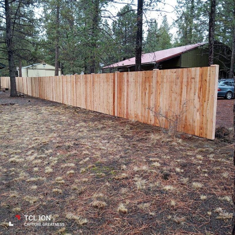 A long wooden fence surrounds a house in the woods.