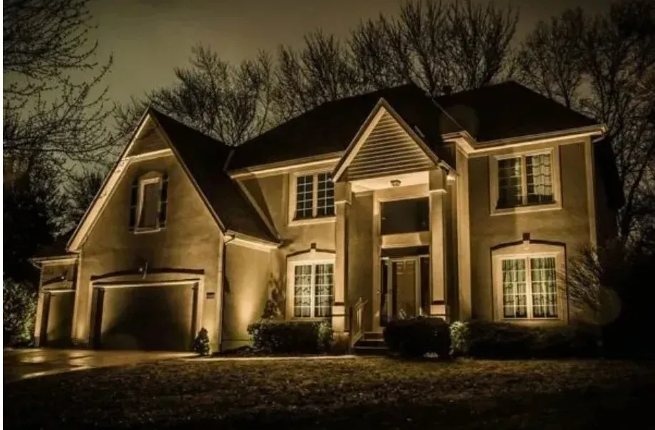 House at night with lights on, trees in the background.