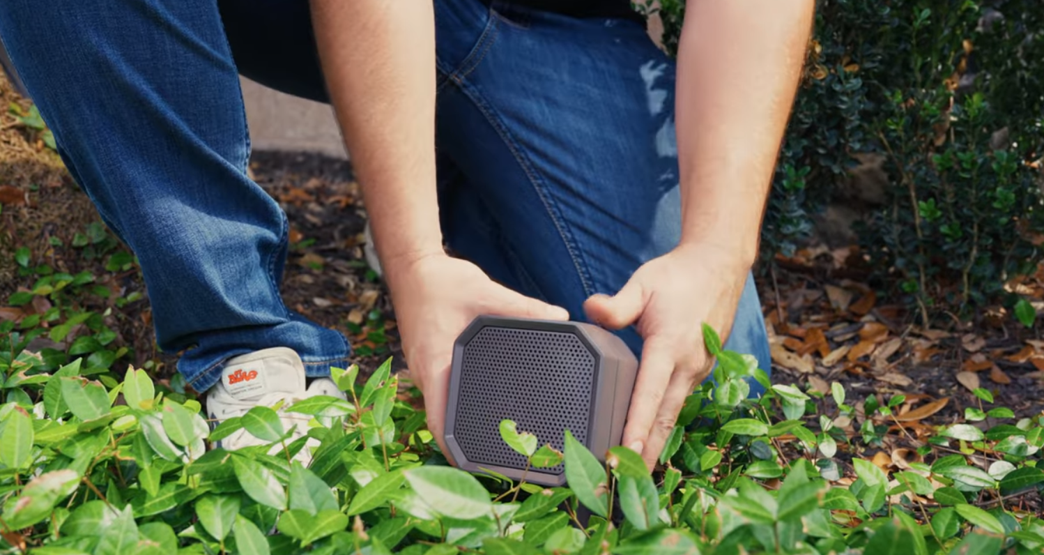 Image of a man installing an AMP Symphony outdoor audio speaker in a bush.