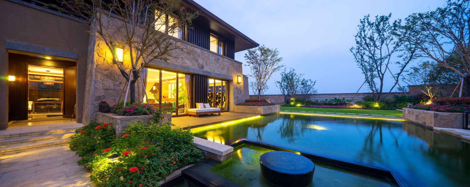 Luxurious modern home at dusk, with a pool, landscaping, and warm lighting.