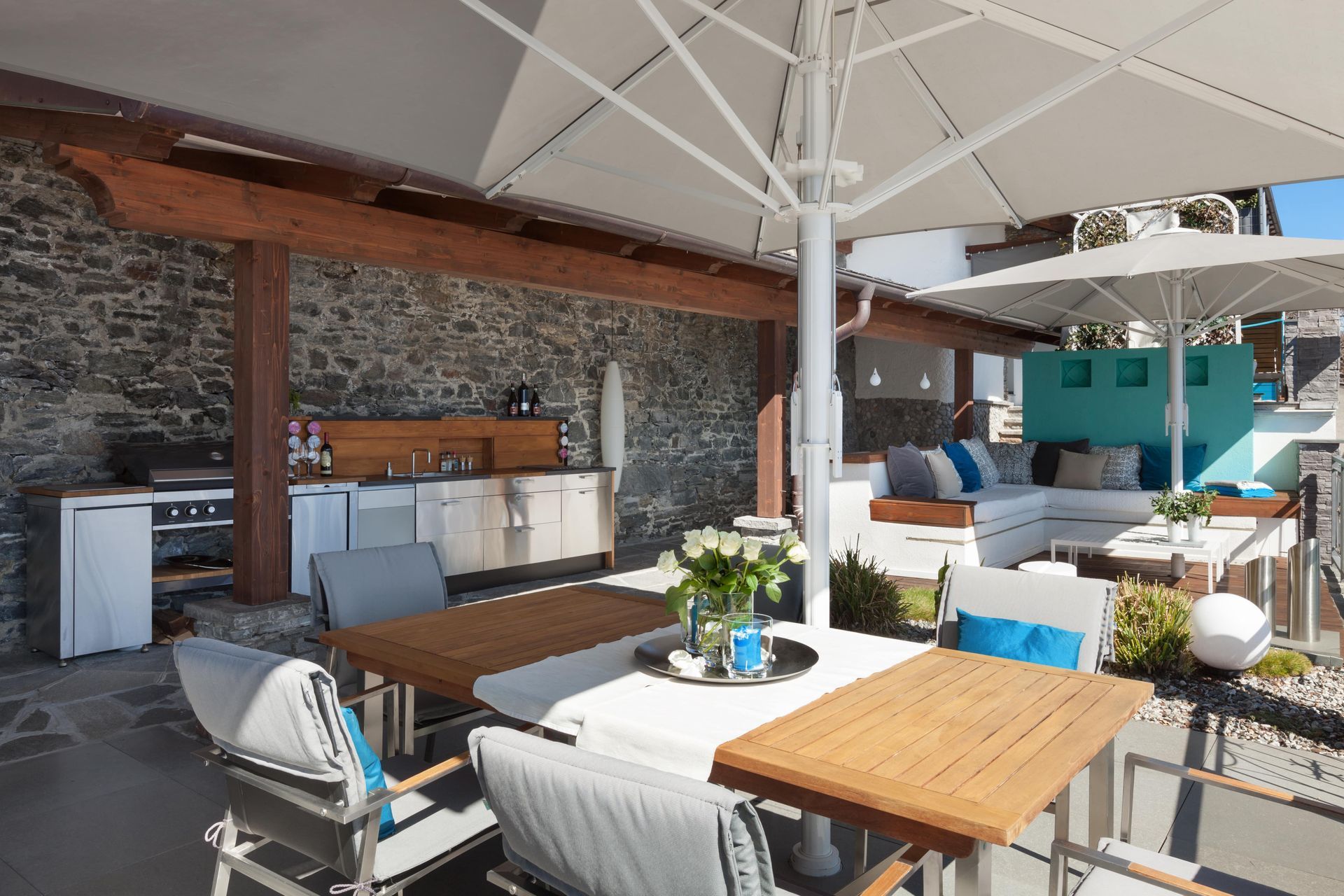 Image of a backyard patio complete with tables, chairs, umbrellas and a couch in the back.