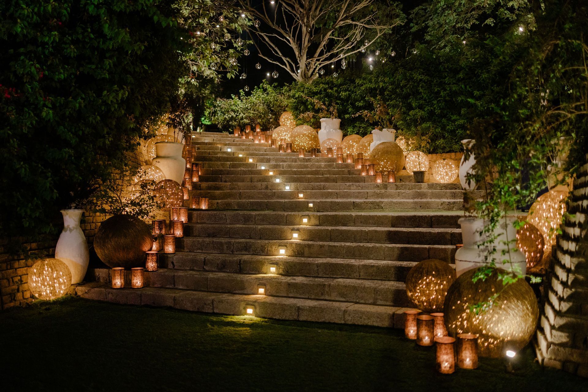 Lit stone staircase at night with candles and glowing orbs leading up to a tree.