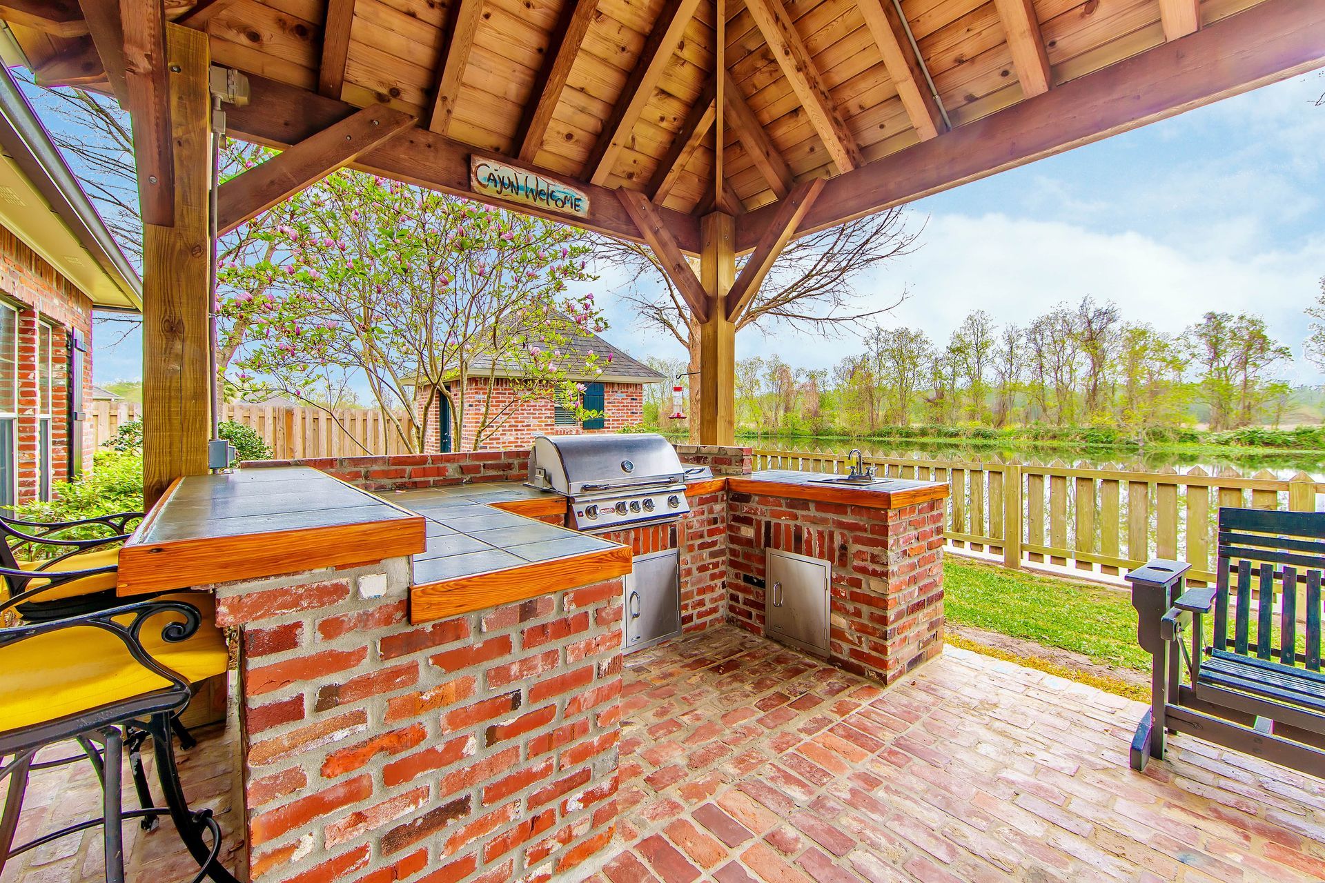 Outdoor kitchen with brick and wood features, grill, countertop, overlooking a body of water.