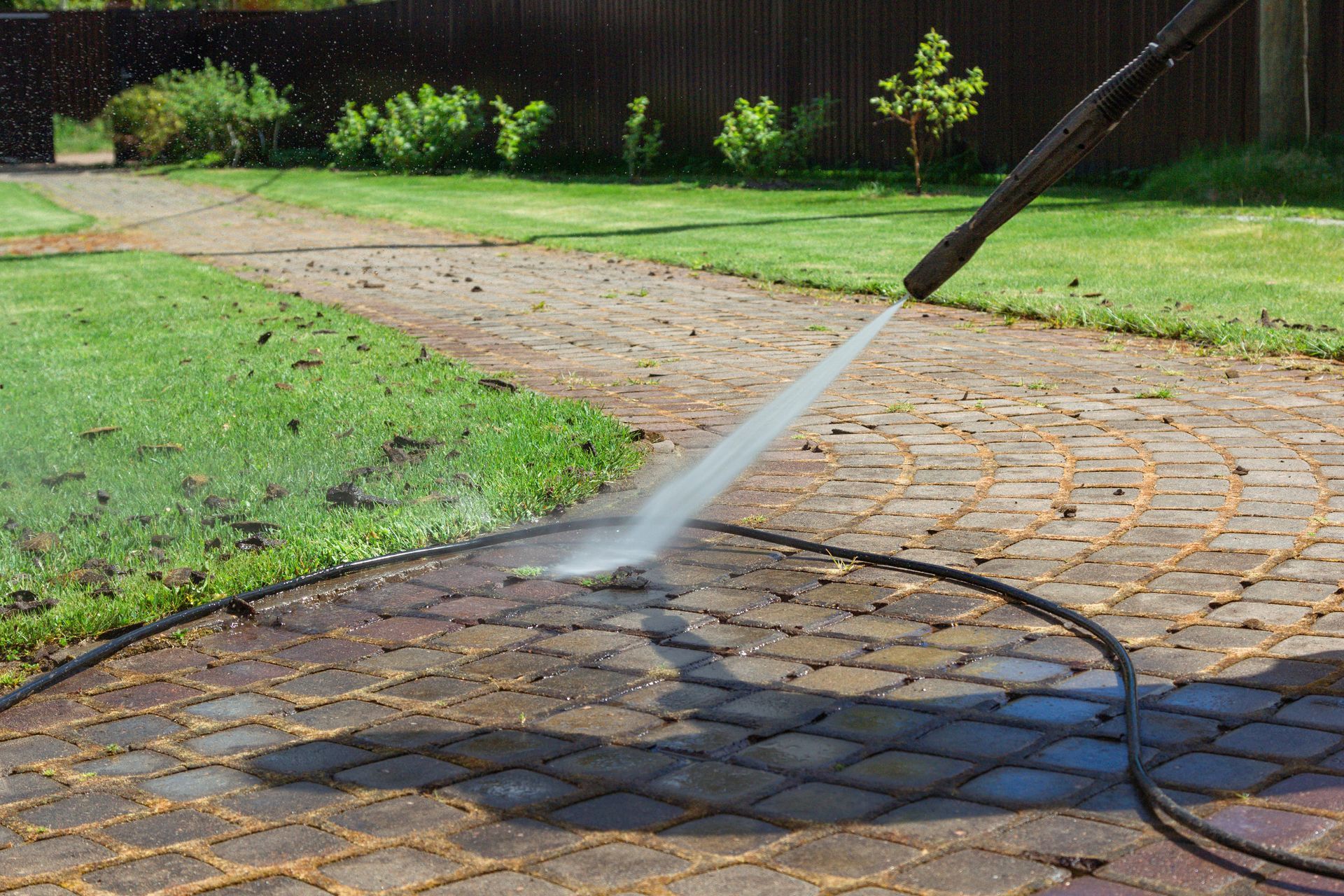 Power washer cleaning a brick patio in a backyard; green grass in the background.