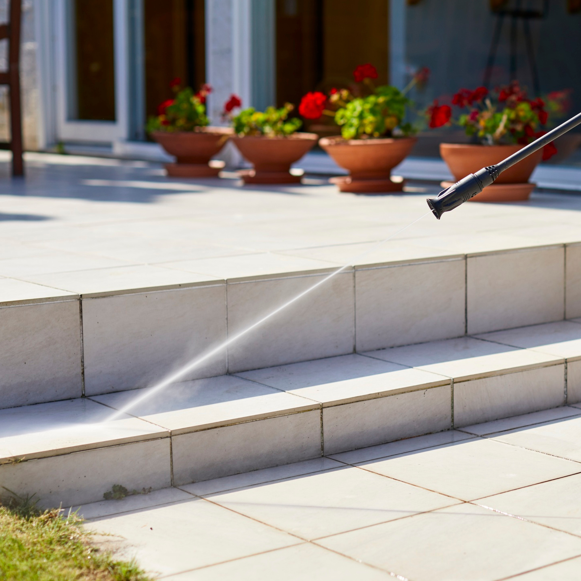 Image of a hose power washing someone's steps to their home with some red flowers in the back.