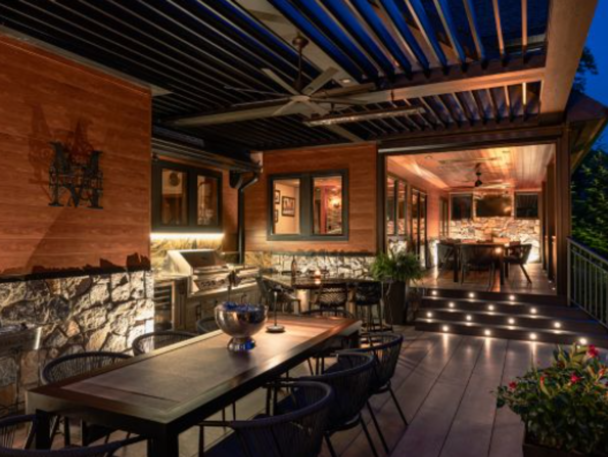 Outdoor patio with dining area, grill, and retractable roof. Warm lighting, stone and wood accents.