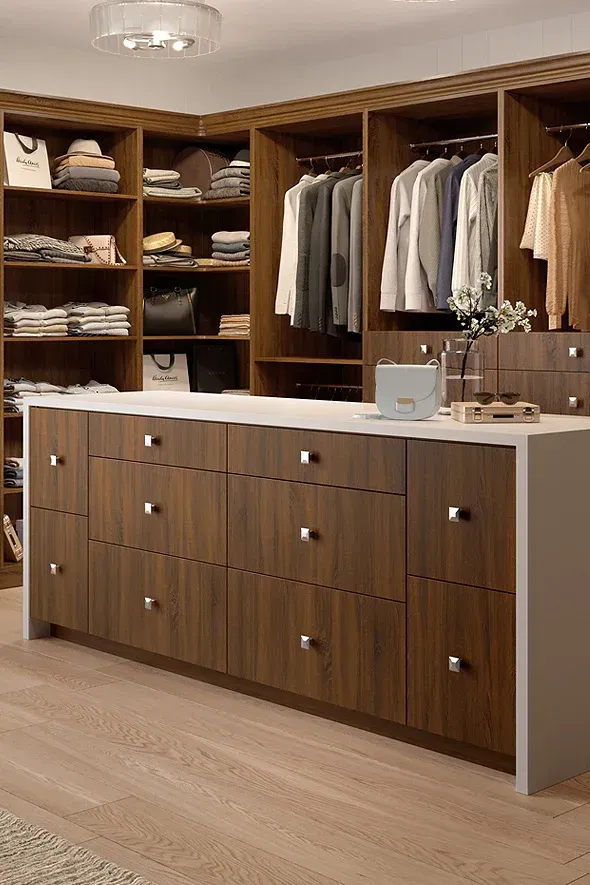 Walk-in closet with brown cabinets, white countertop island, and hanging clothes.