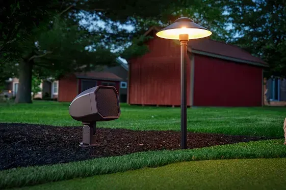 Lawn with an illuminated lamp post and speaker. Red barn in background.