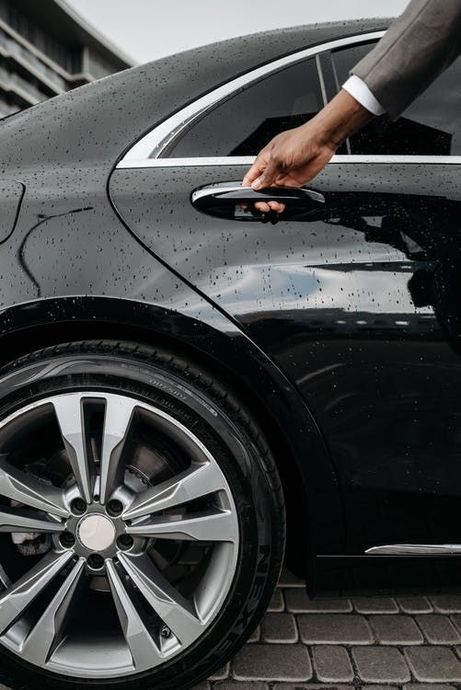 A man in a suit is opening the door of a black car.
