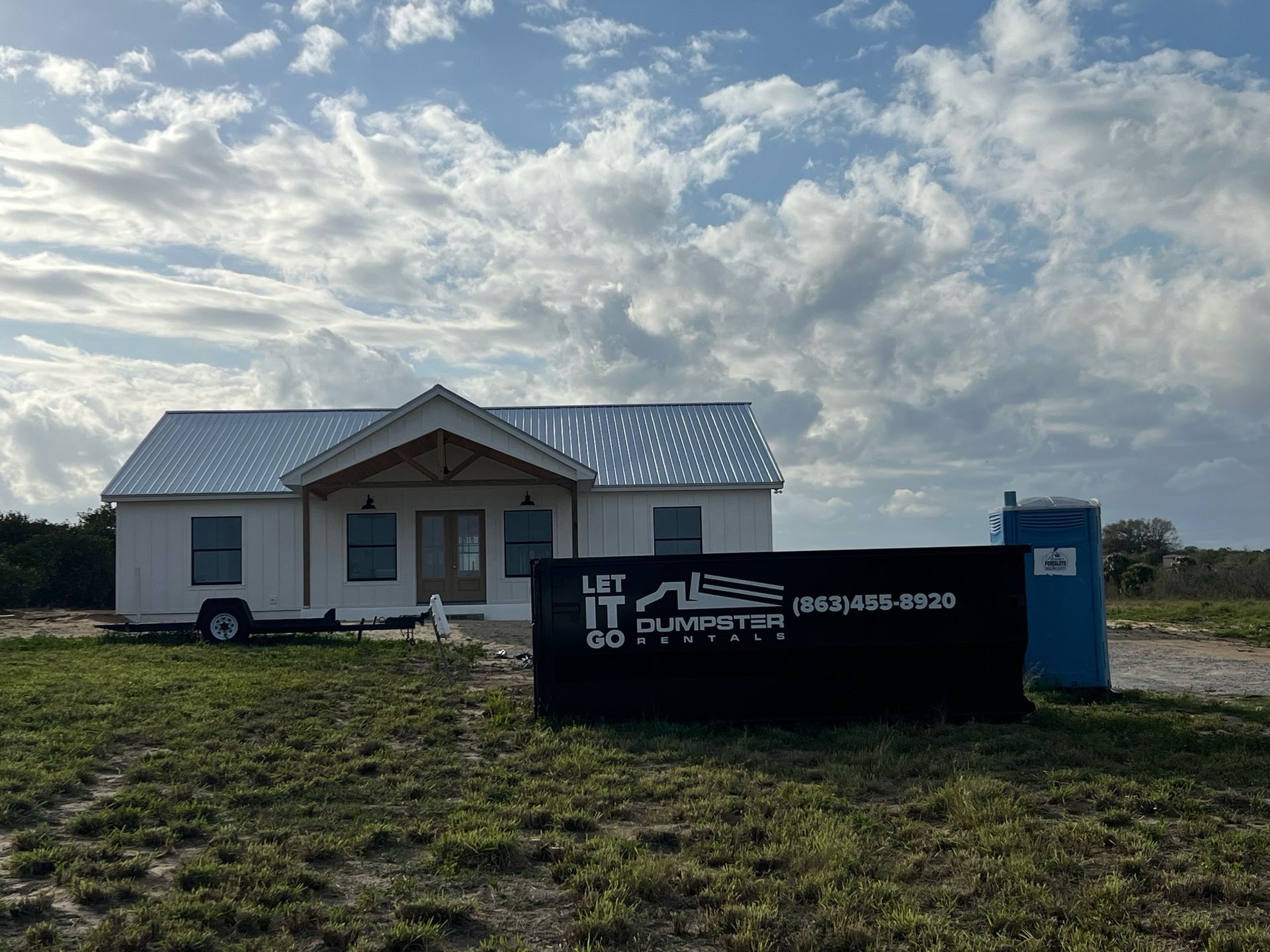 A small white house is sitting in the middle of a grassy field.