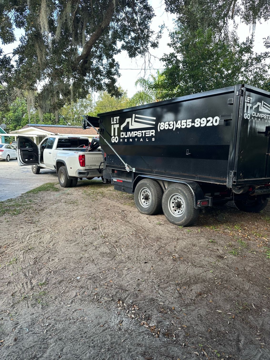A dumpster is parked next to a truck in a dirt lot.