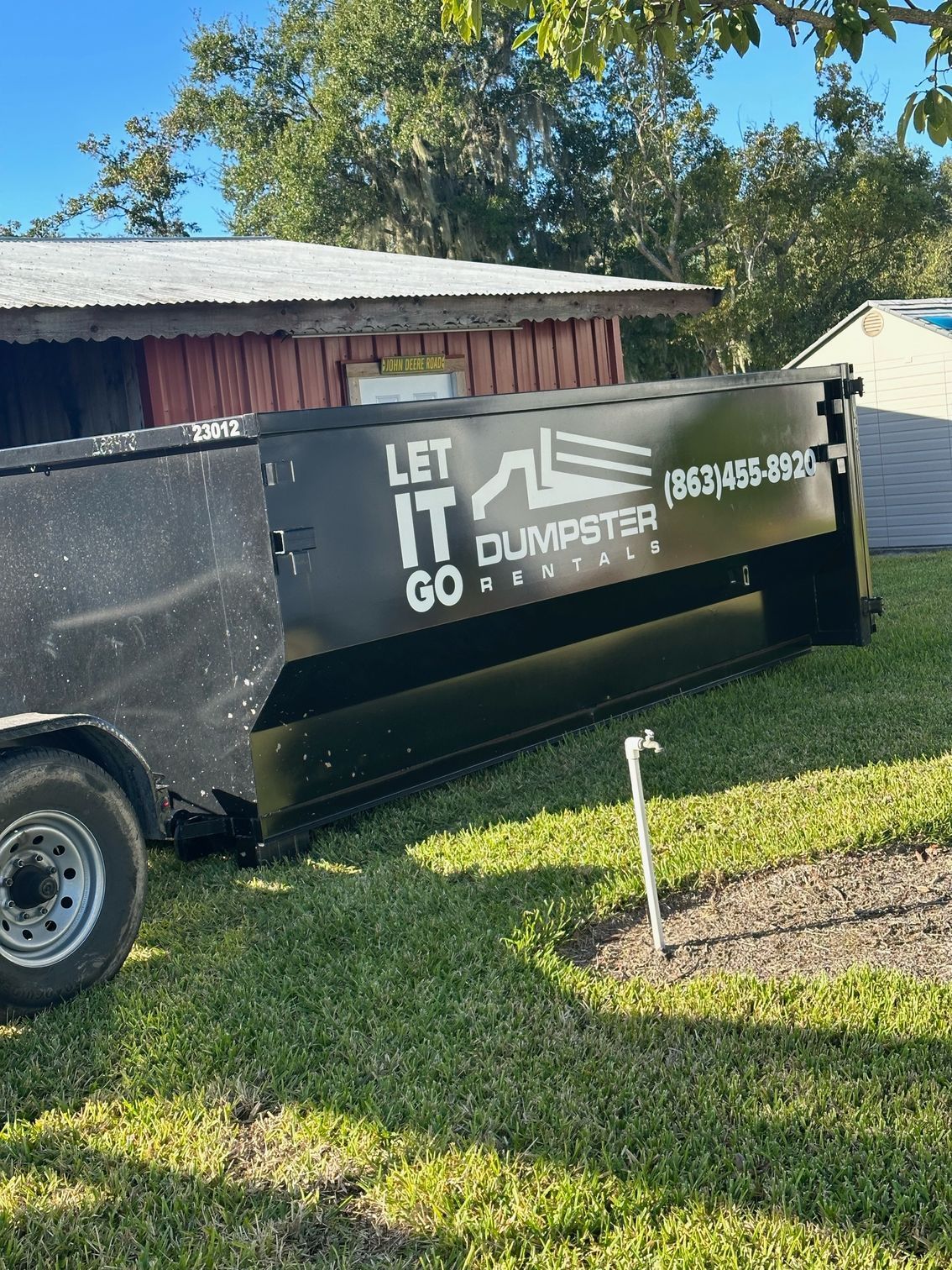 A dumpster is parked in the grass next to a trailer.
