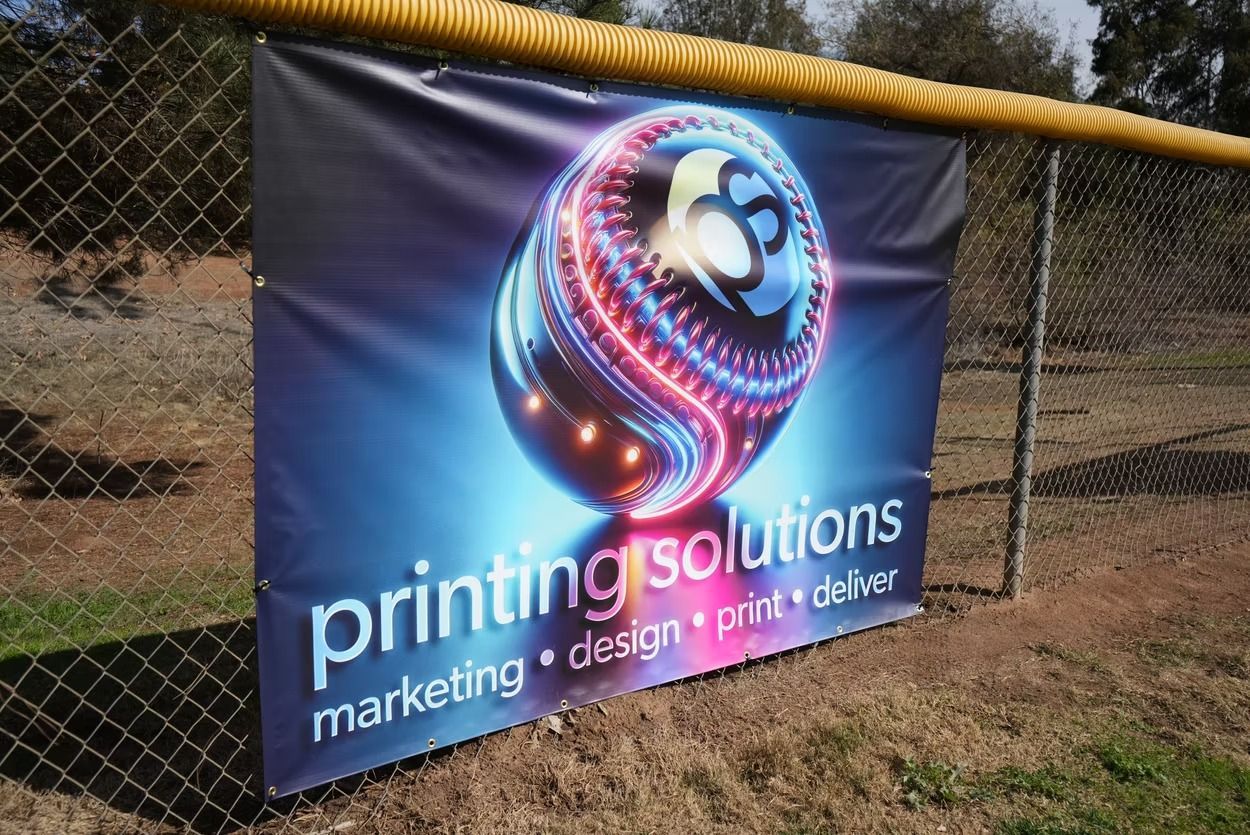 A printing solutions banner is hanging on a chain link fence