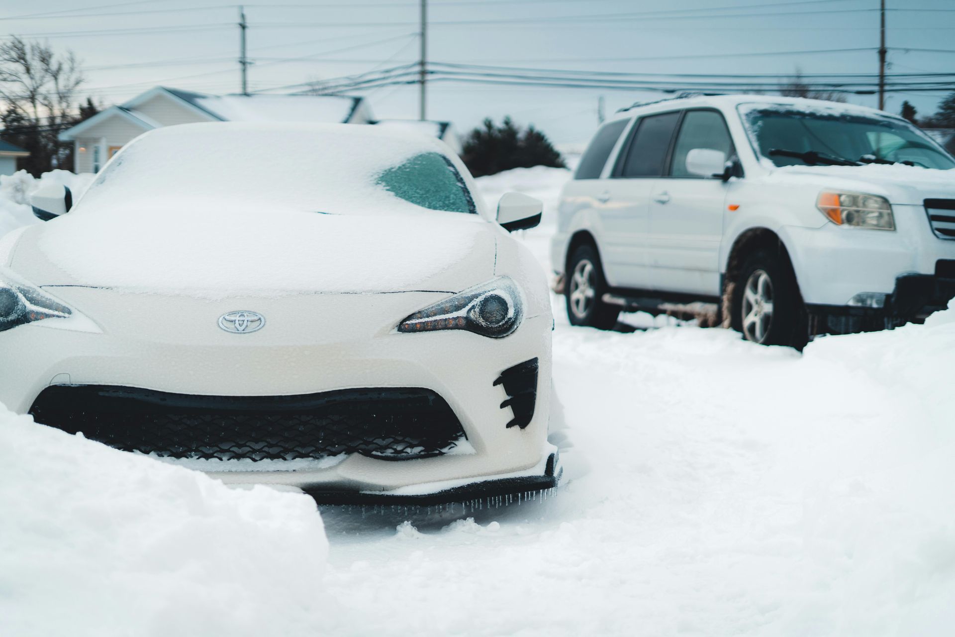 A car parked outside is not starting due to the cold weather. Snow covers the front of the car. 