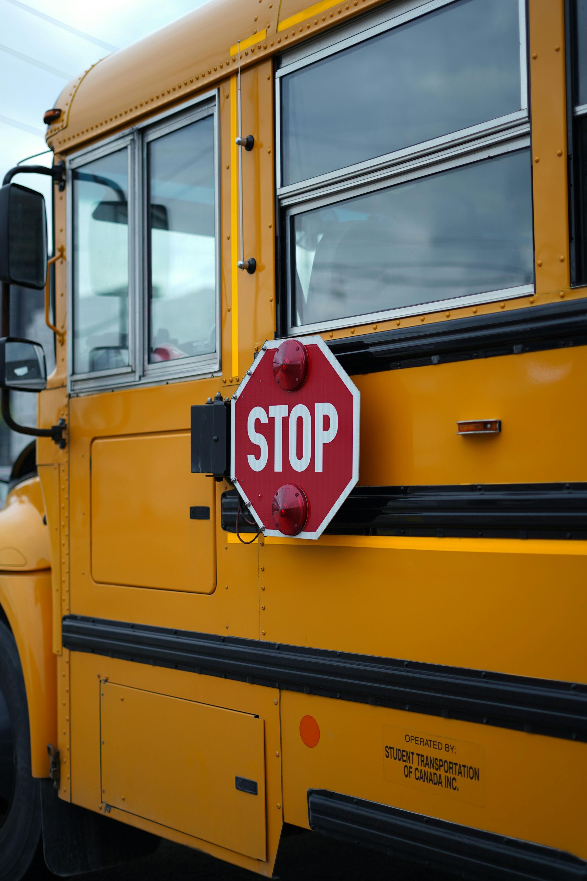 The red stop sign with lights on the driver's side of a yellow and black school bus.