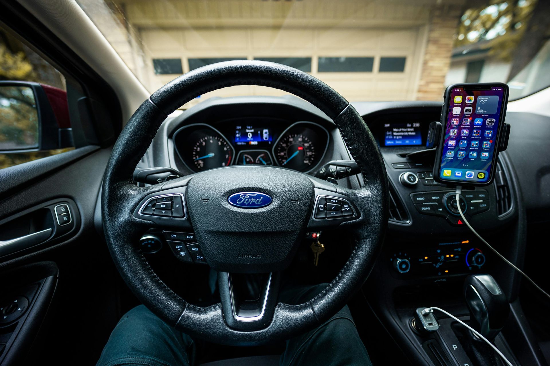 The view from the front seat of a car There is a phone holder with an iPhone near the car's radio. 