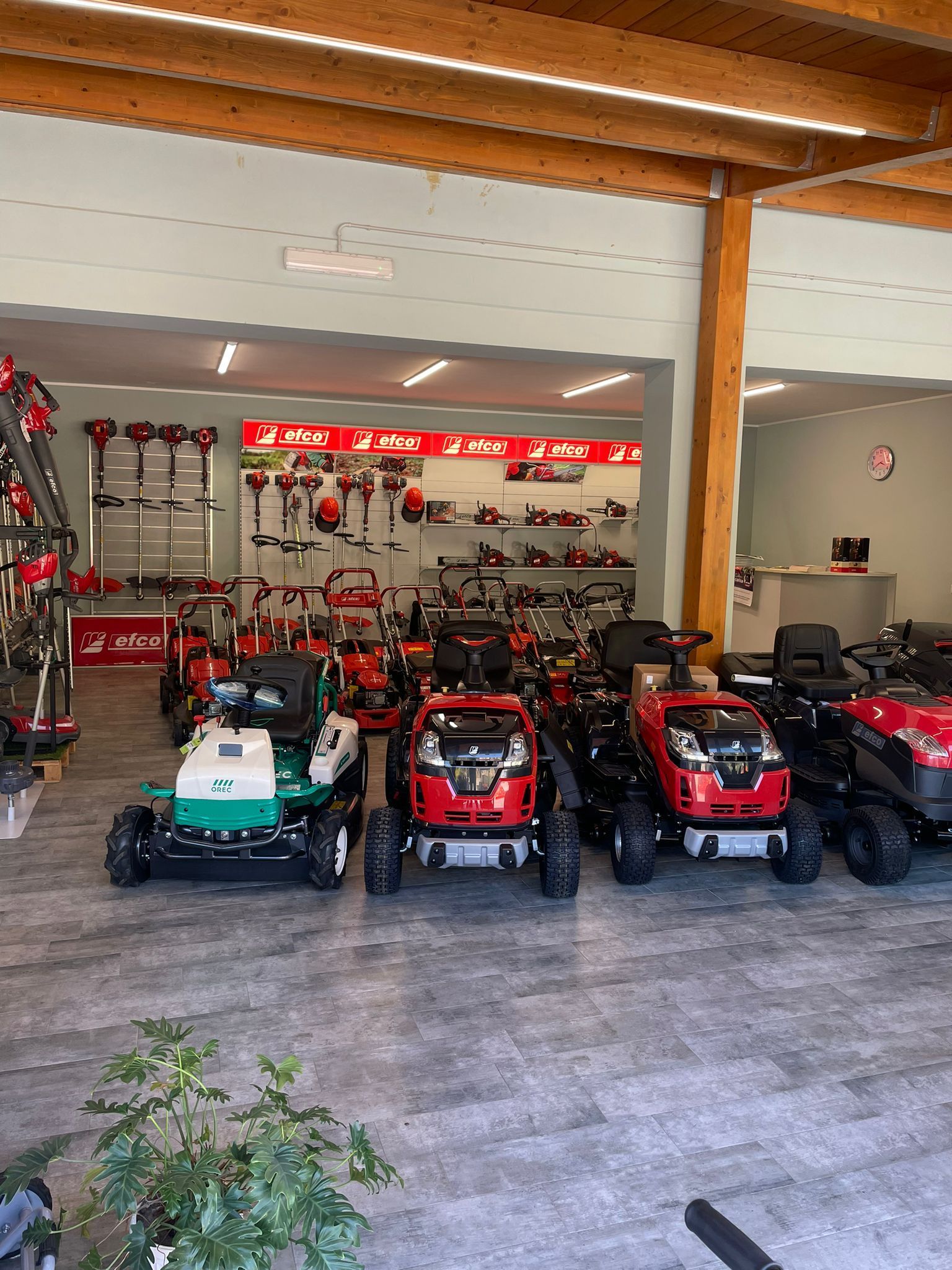 Showroom al coperto con diversi trattorini rasaerba rossi, verdi e neri esposti in fila