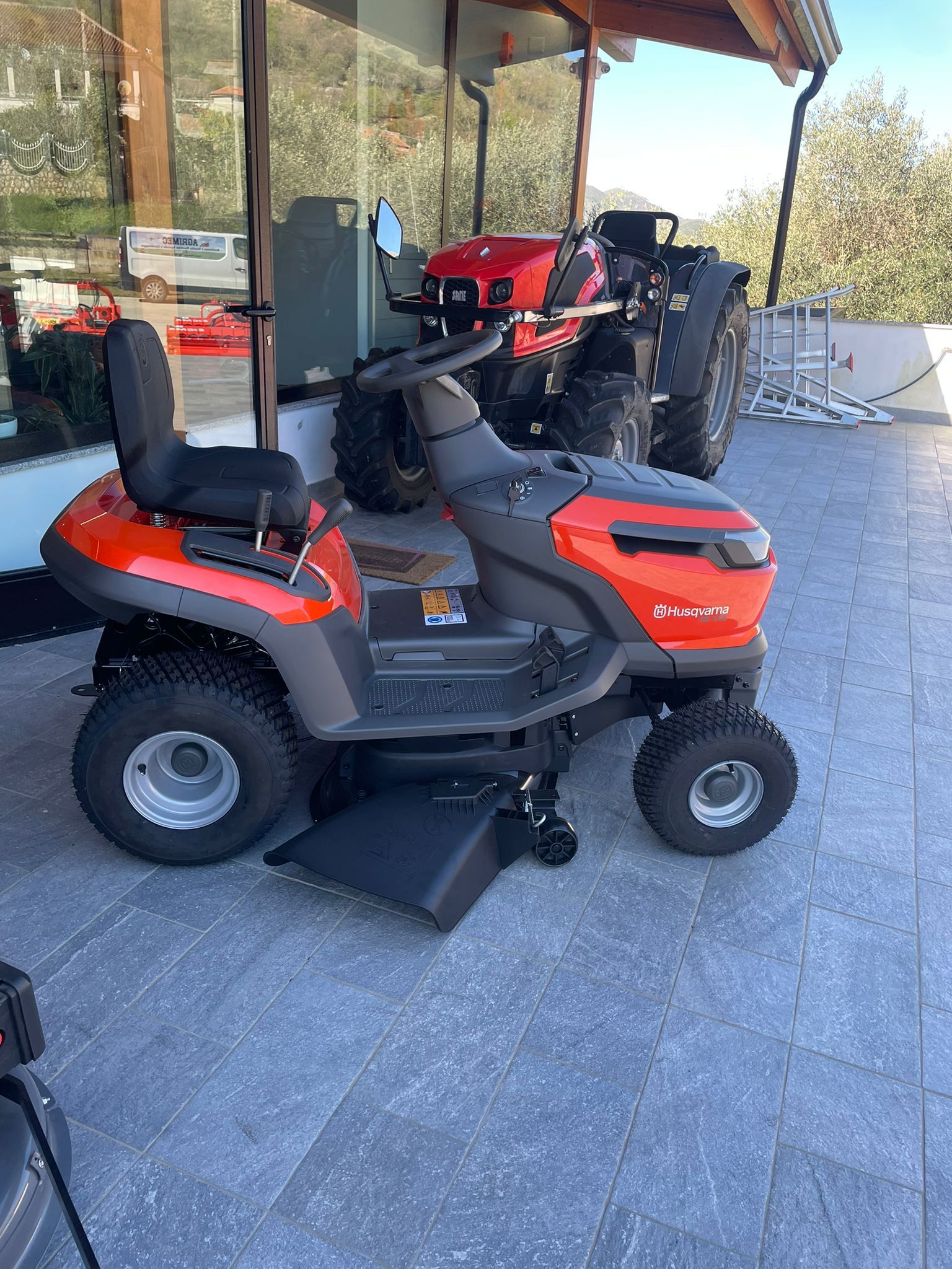 Un tosaerba rosso a motore è parcheggiato su un patio in pietra accanto a un portico coperto.