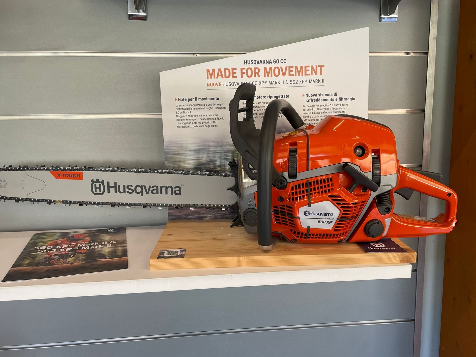 Motosega Husqvarna arancione su uno scaffale con un cartello informativo del prodotto alle sue spalle.