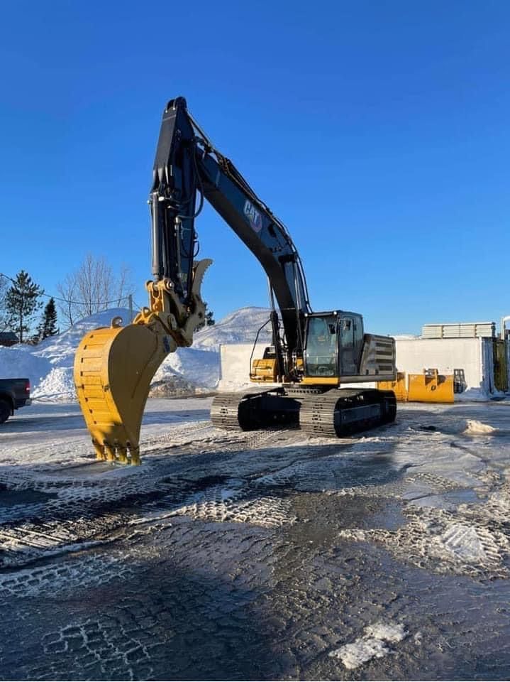 Excavatrice Caterpillar jaune sur chenilles dans un parking enneigé et ensoleillé.